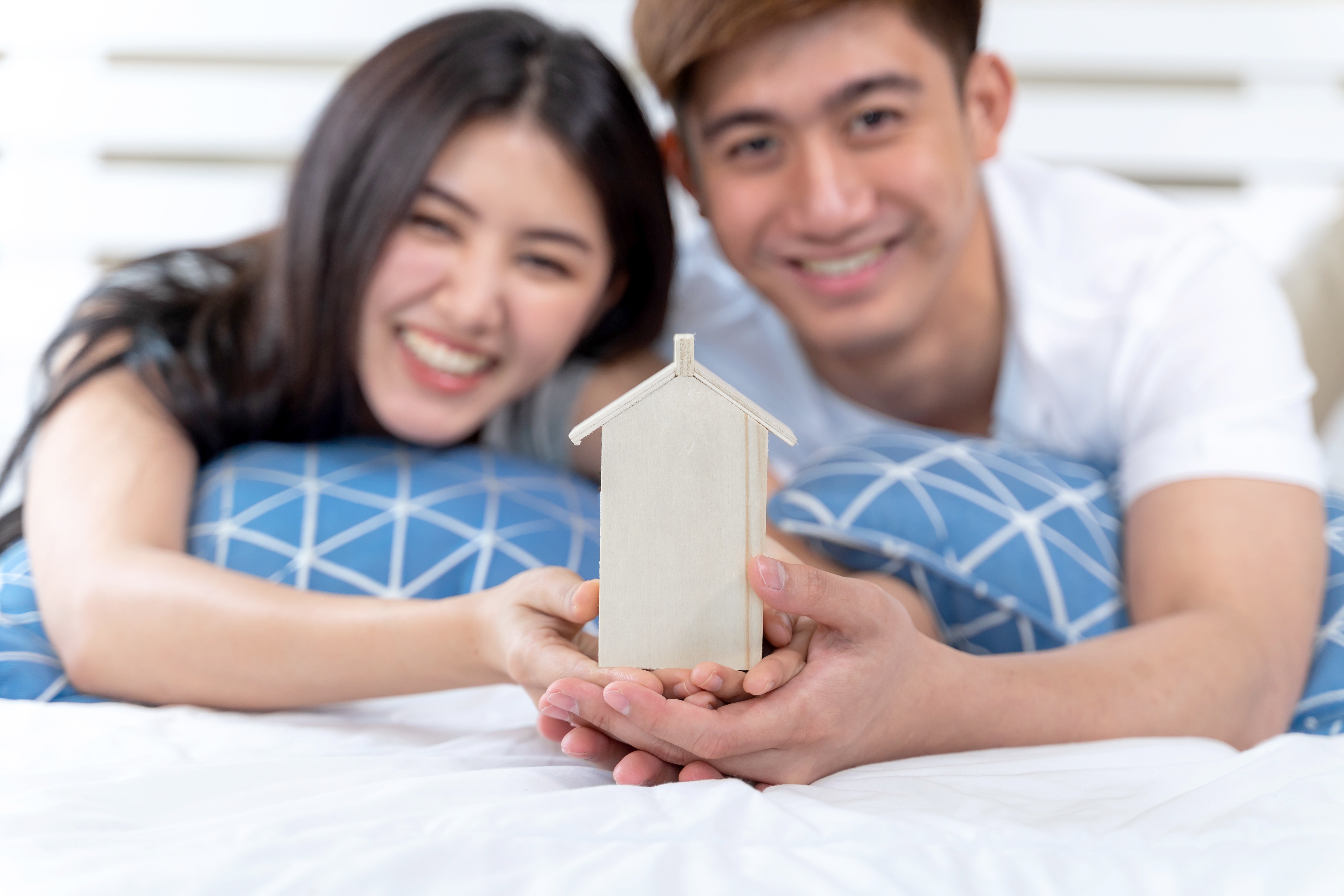 young-couple-holding-house-toy-on-the-bed
