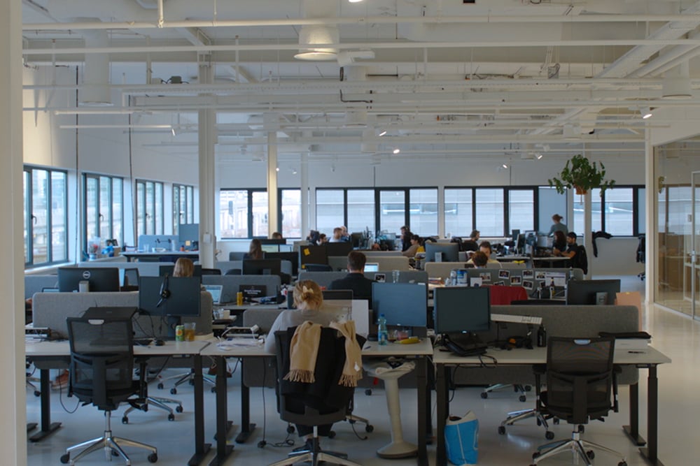 It's a picture of an open space office with people sitting at different tables and working.