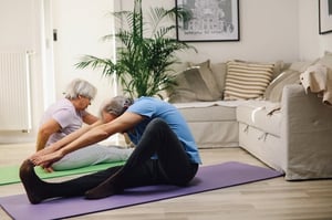 older couple stretching together on living room floor