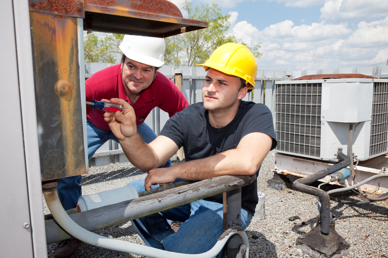 Construction workers maintaining HVAC systems on a rooftop.