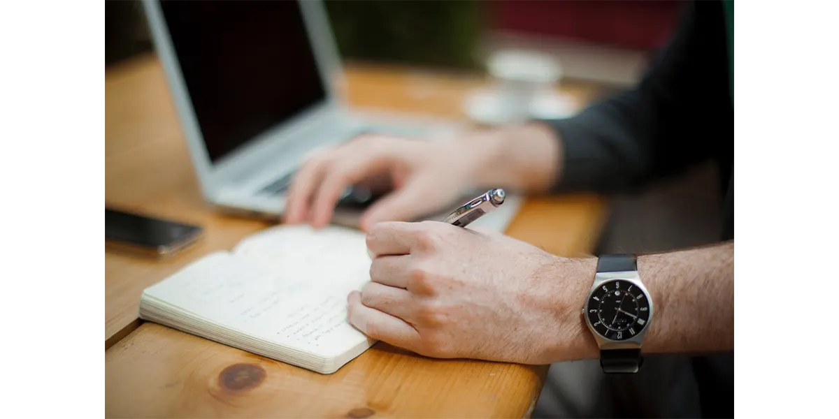 hand writing a list by a laptop