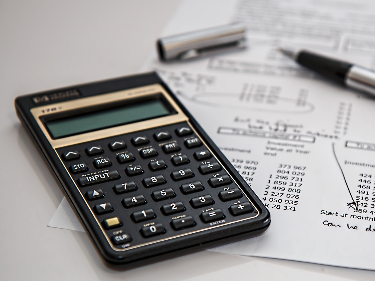 Black calculator near pen on white paper