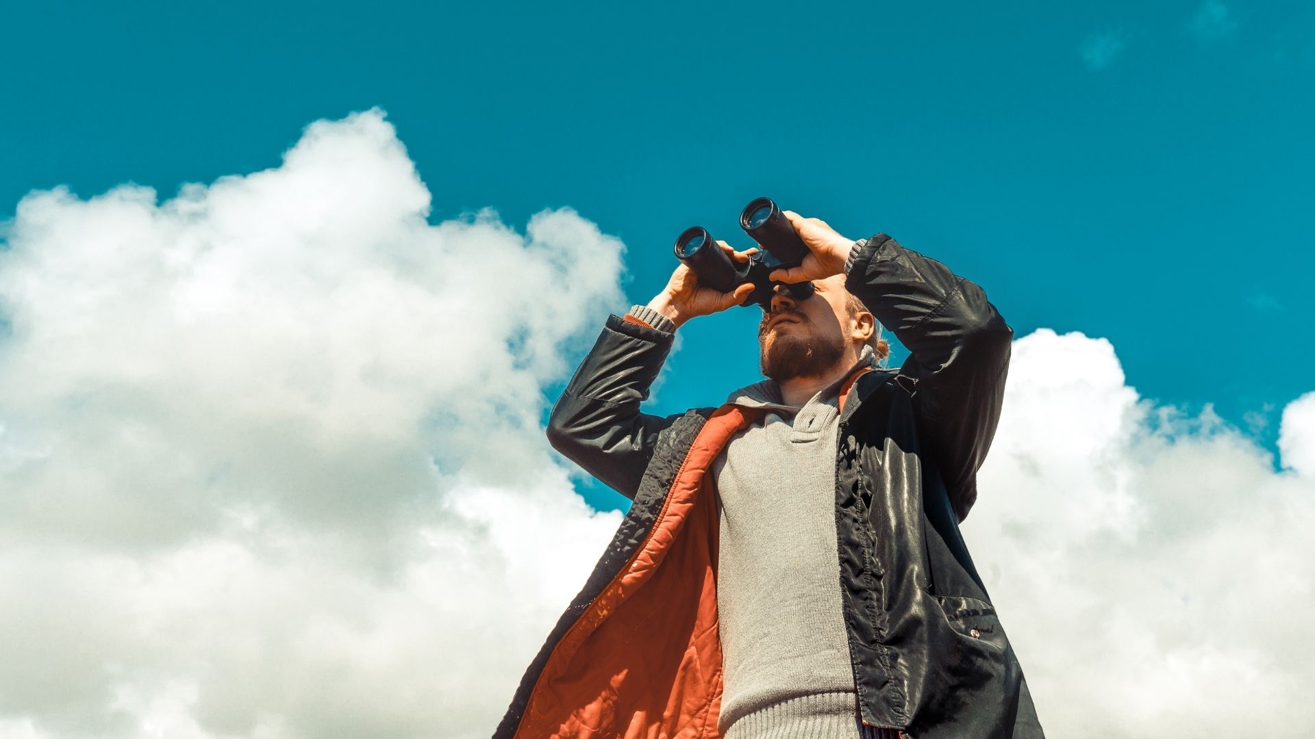 Man looking through binoculars on blue sky