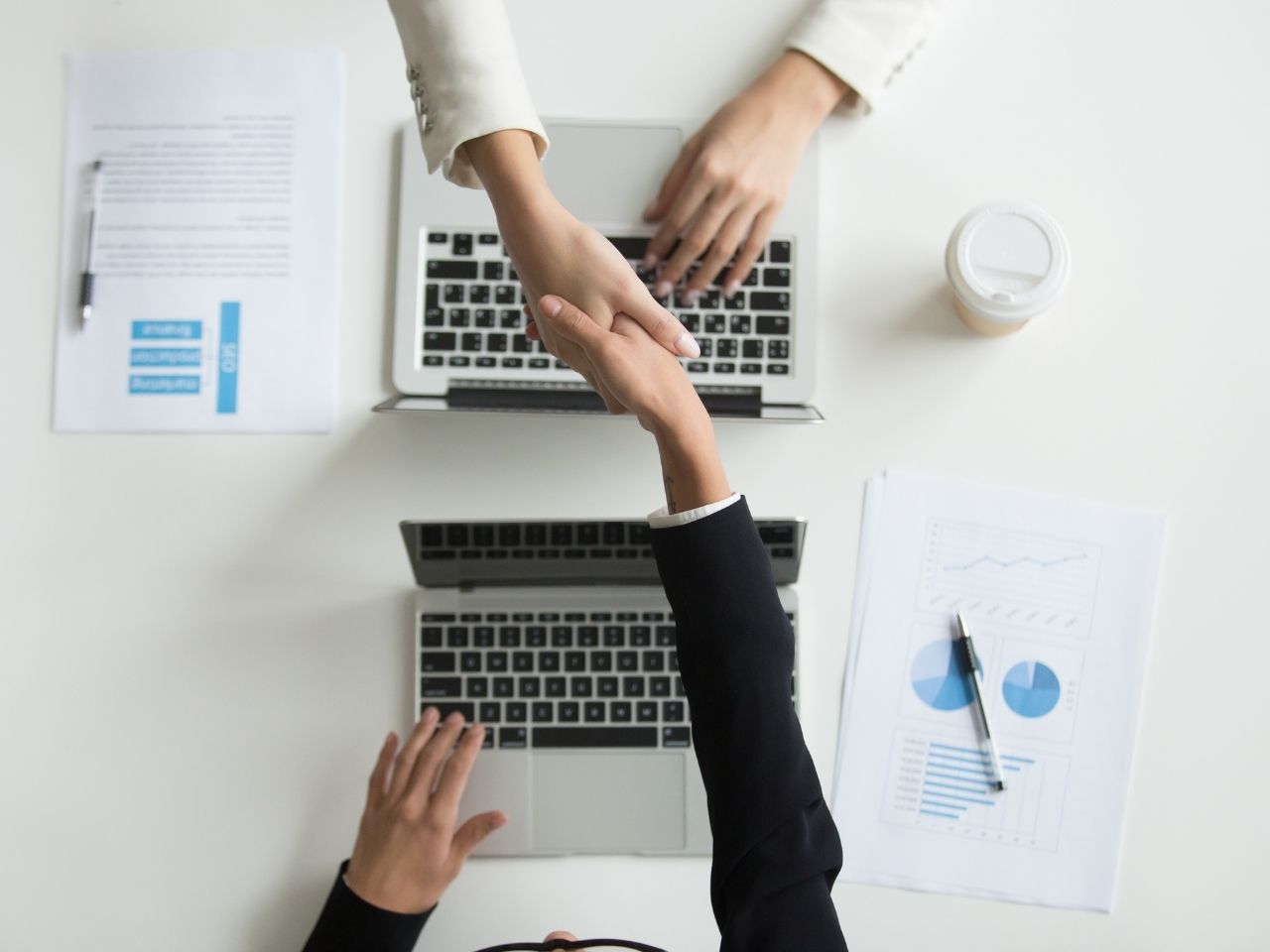 Two people shaking hands over laptop