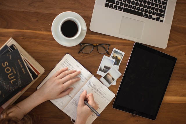 Person writting on a notepad and drinking coffee