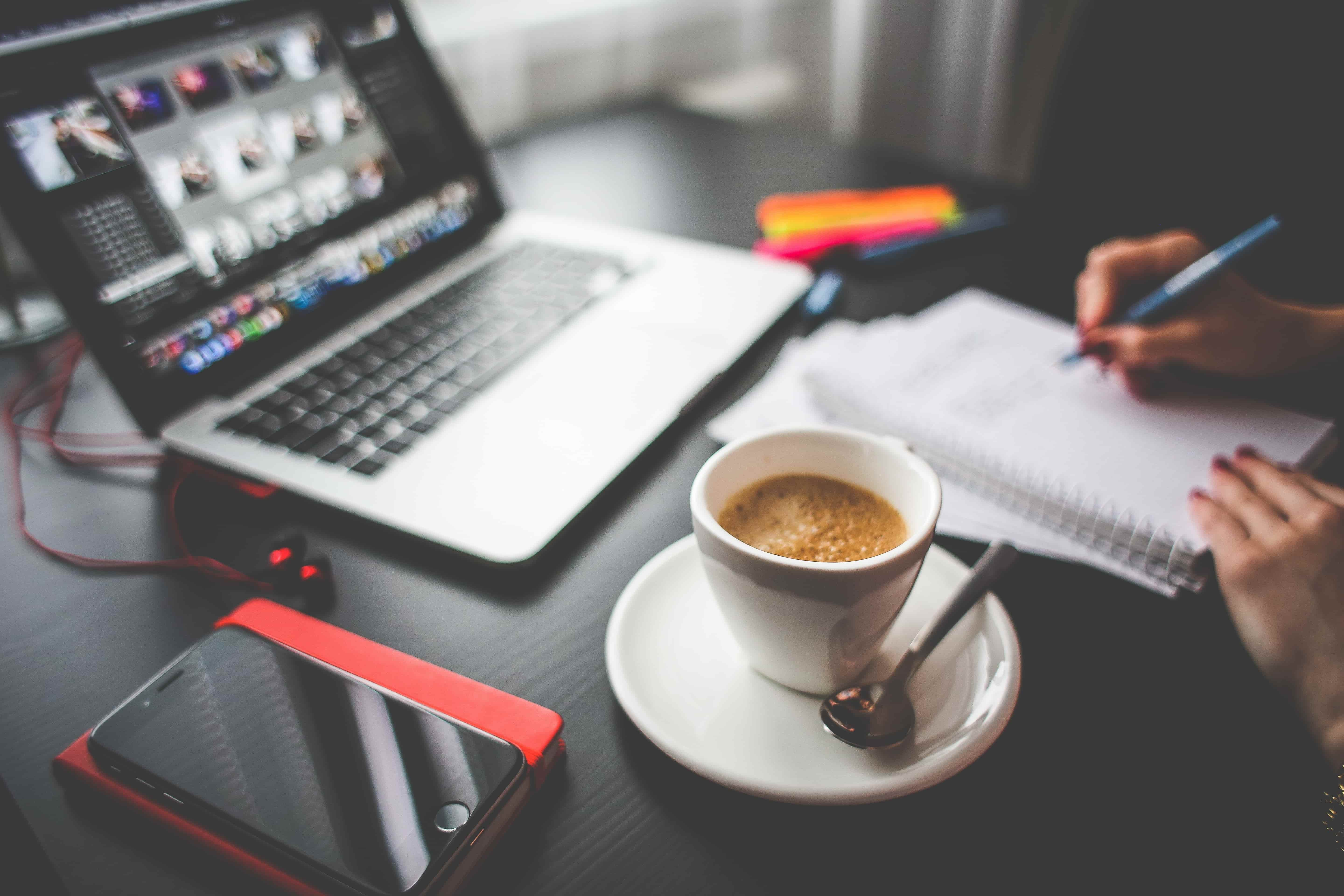 Person writing on paper with coffee and MacBook