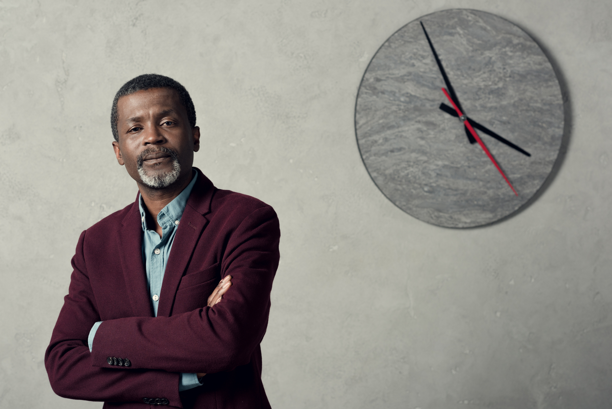Confident african american businessman with crossed arms standing near wall with big clock