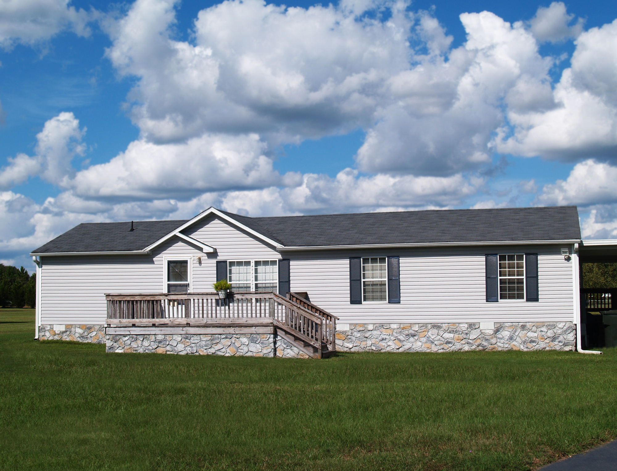 Gray trailer home with stone foundation or skirting and shutters in front of a beautiful sky