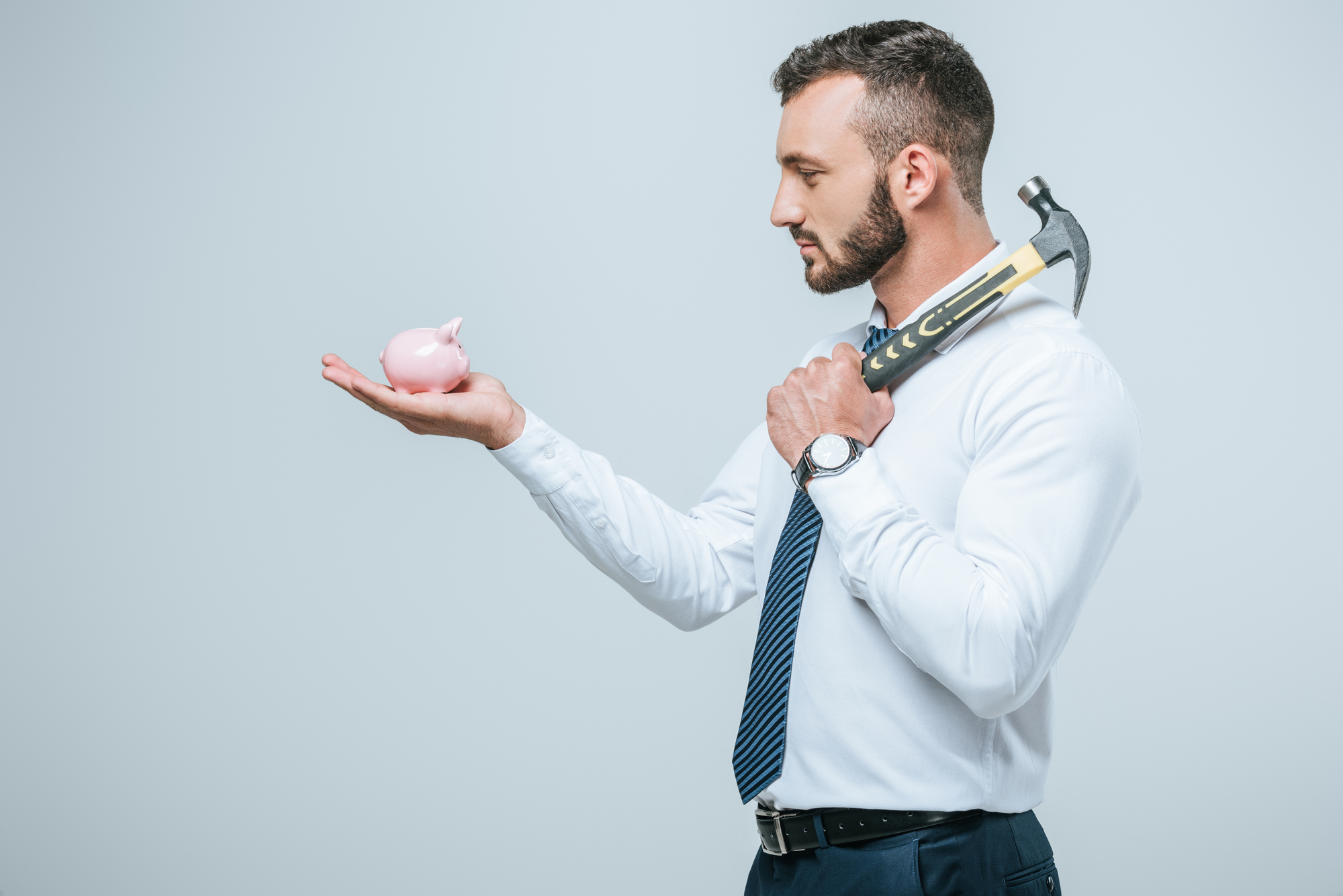 Side view of financier holding piggy bank and hammer isolated on grey