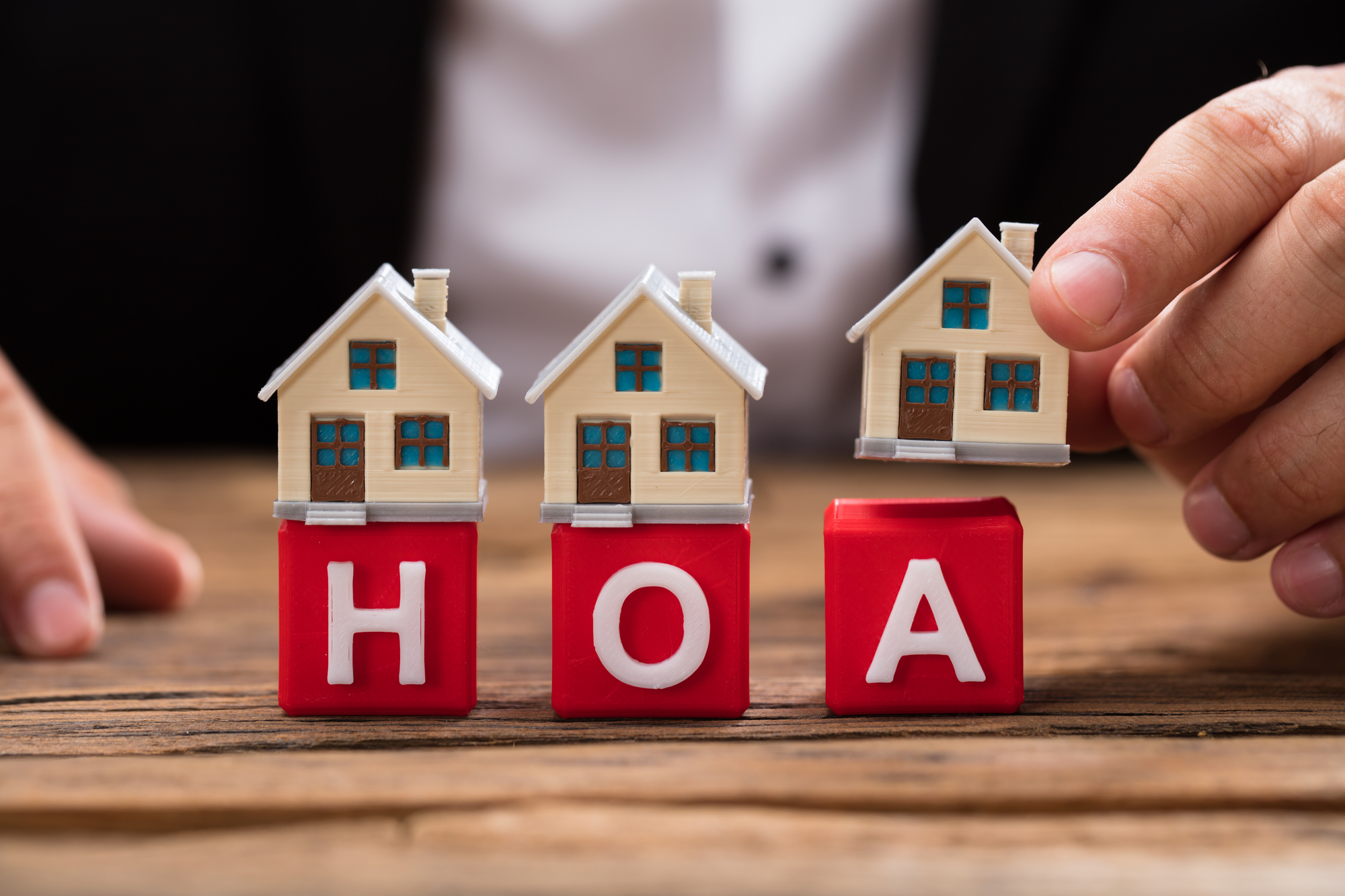 Businesspersons hand placing house model over red HOA blocks on wooden desk